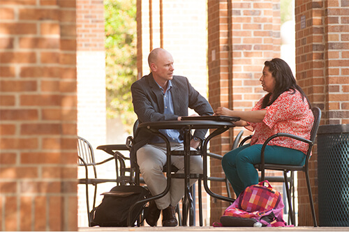 Photo of philosophy professor and student sitting outside library talking about philosophy course.
