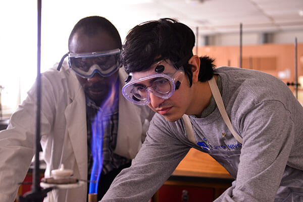 George Anqandah, Ph.D., looks on as student ignites Bunsen burner.
