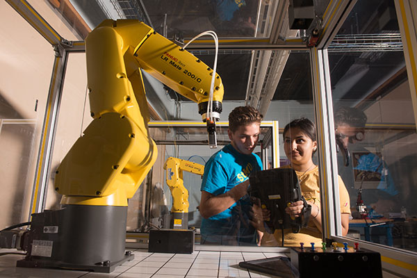 Students operate robotic arm in Industrial Engineering lab.