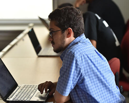 Male history student in classroom with his laptop listening to professor.