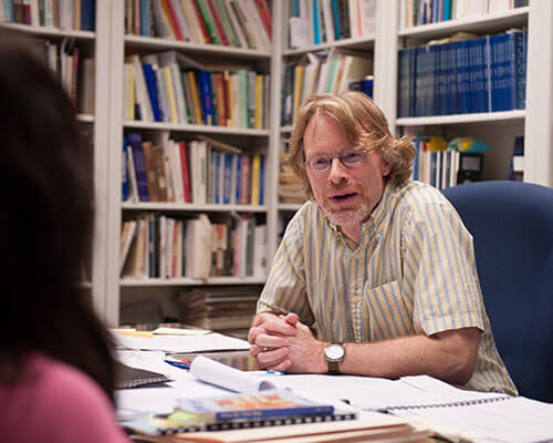 Theology professor speaks to a student in his office.