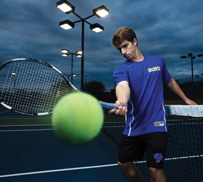 Tennis player Michael Maciel on the St. Mary's tennis courts with a racket hitting a tennis ball toward the camera