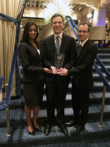 Three students stand with trophy