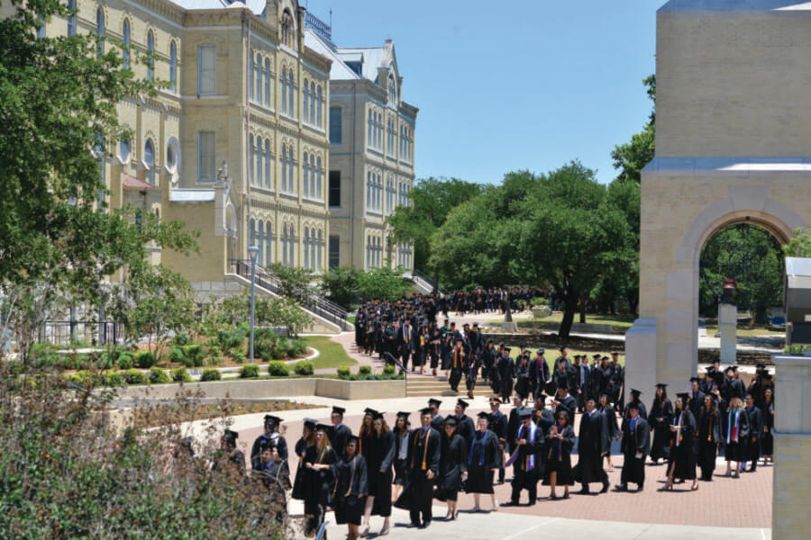 Students in regalia process by the Bell Tower to their commencement.