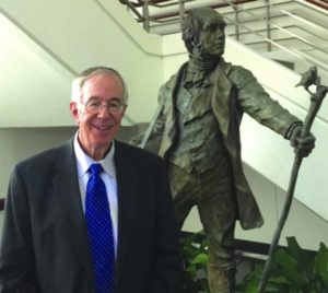John Haught stands by a bronze statue