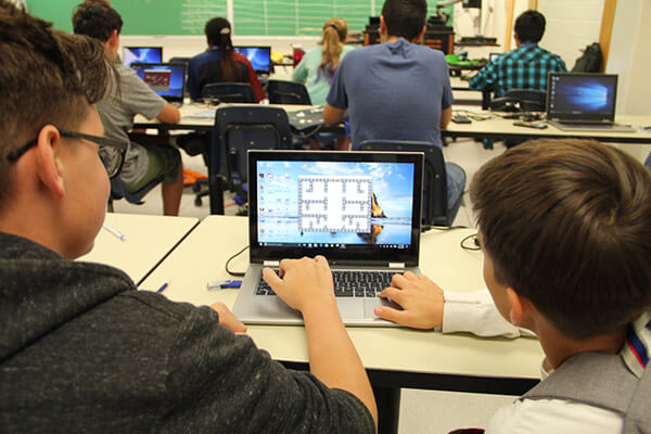 Two middle school students face a computer screen showing a game they have built together