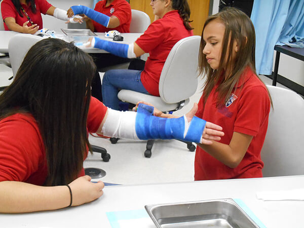 A female camper wraps a fellow camper's arm in medical tape