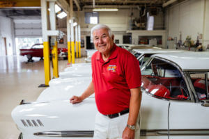 Car collector stands in front of his cars in his garage.