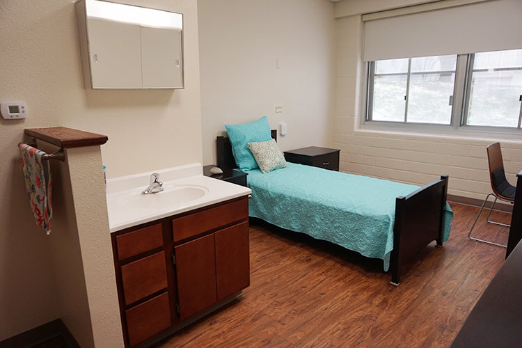 A single bedroom in Chaminade Hall, showing a twin bed and a sink