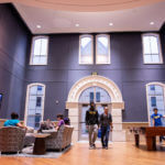 Wide view of a two-story common room in Founders Hall, featuring a seating area and a pool table