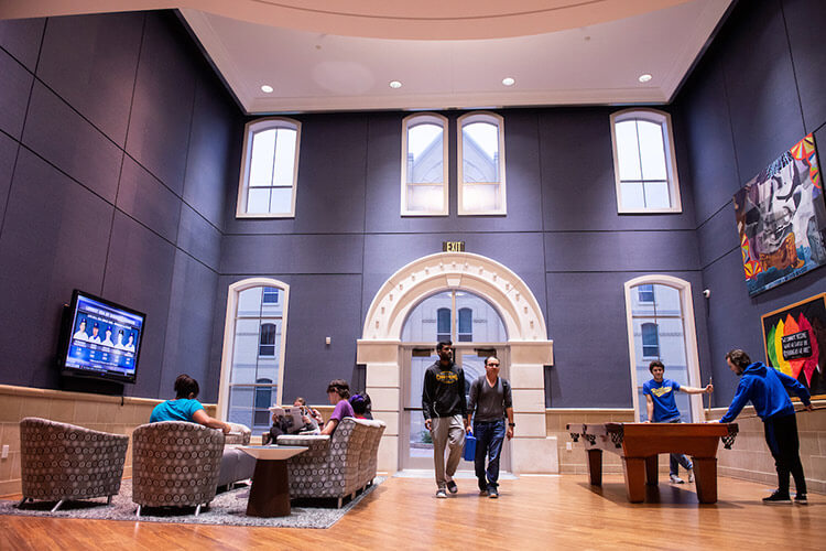 Wide view of a two-story common room in Founders Hall, featuring a seating area and a pool table