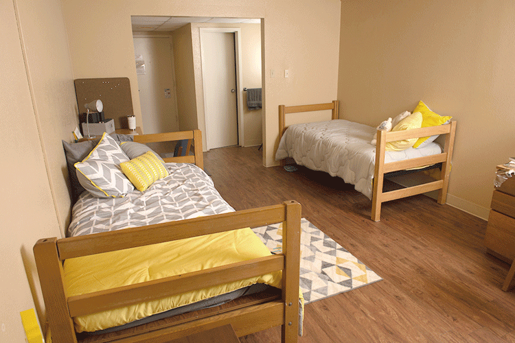 View of a Lourdes bedroom, showing two beds and the entryway in the background