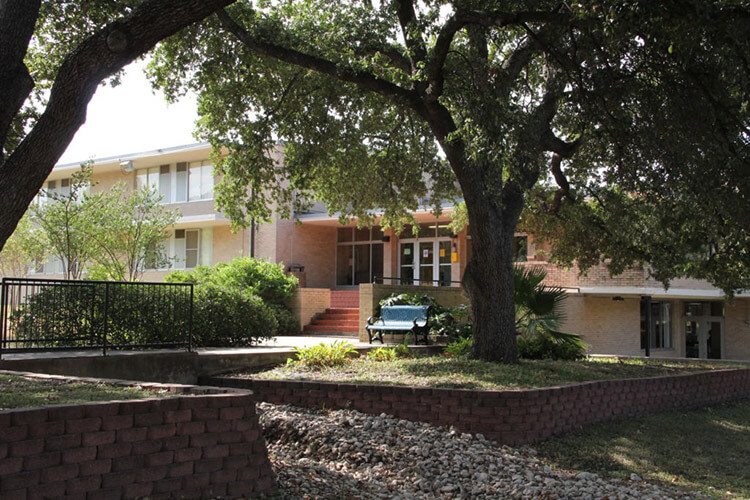 Front entrance of Marian Hall, a brick building with mature shade trees