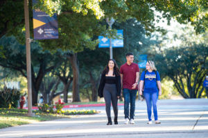 Three students chat as they walk across campus.