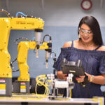 A female engineering student uses a robotic arm to work in a lab.