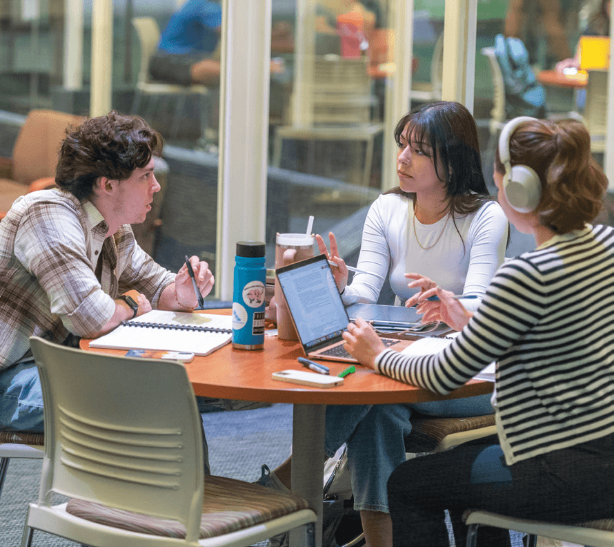 Three students sitting at a round table working on their assignments.