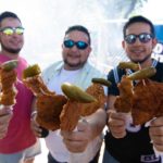 Three people show off their Chicken on a Stick at Fiesta Oyster Bake at St. Mary's University