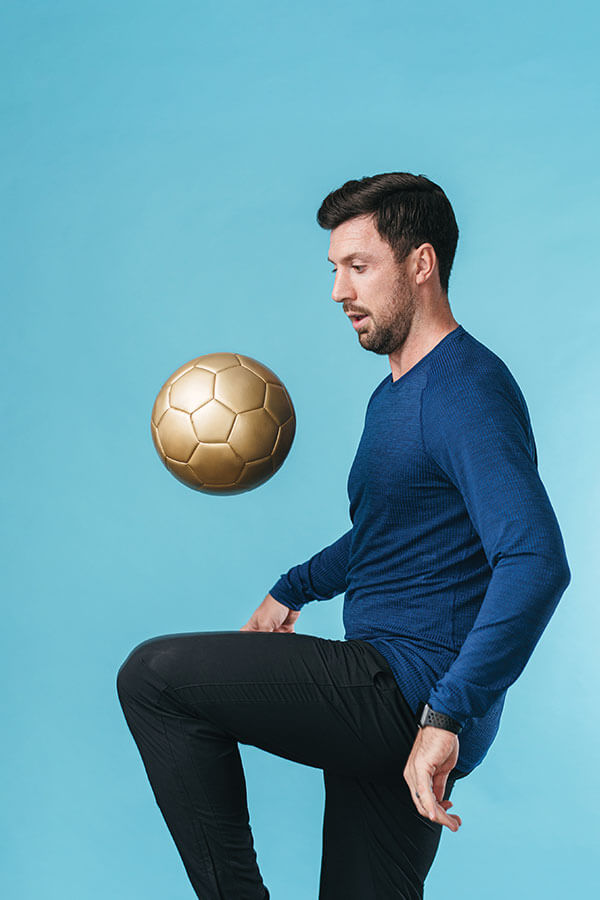 Johnny Clifford, Men's Soccer Head Coach, balances a gold soccer ball in the air.