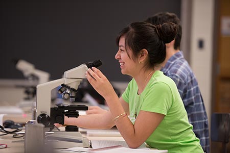 female student in green shirt using microscope and smiling