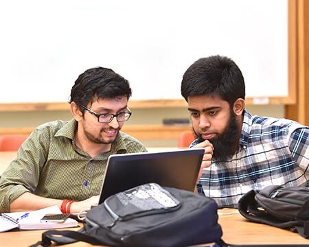 two male cybersecurity students working on laptop