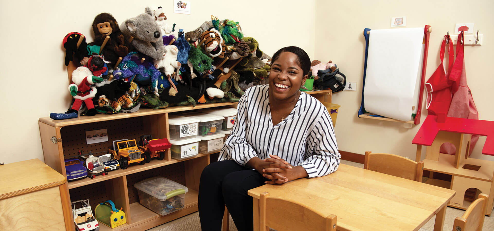 counseling student sits at a child-sized table surrounded by toys and stuffed animals
