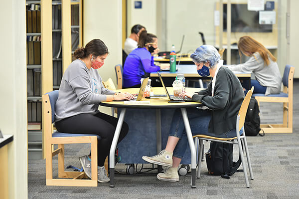 Students studying together in the Commons, wearing facemasks. 