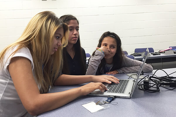 Three female students work together on a laptop during  Python for Data Analytics camp.