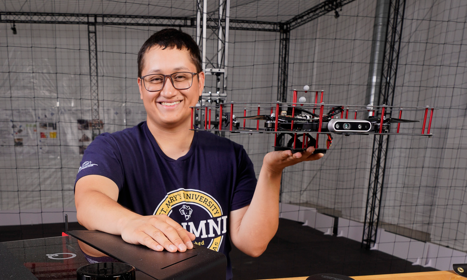 Engineering students smiles as he holds up a drone.