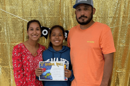 Alexandria "Lexi" A. Rubio poses with an A honor roll sign with her parents.
