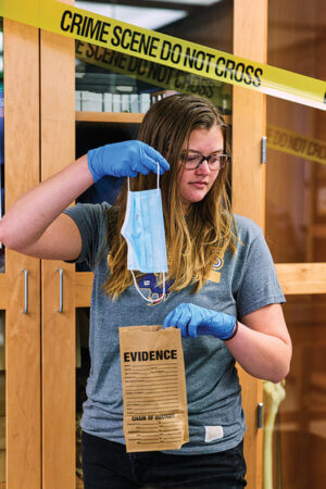 A forensic science student puts a piece of evidence in a bag in a classroom lab