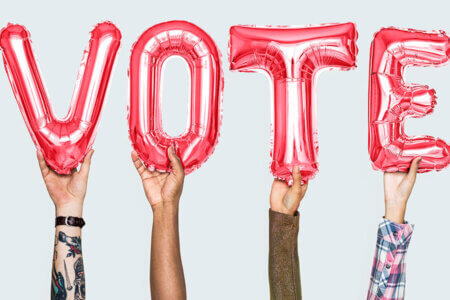 Four hands hold up balloons spelling vote.