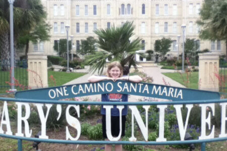 Lily Schow stands in front of the St. Mary's University sign at age 10.
