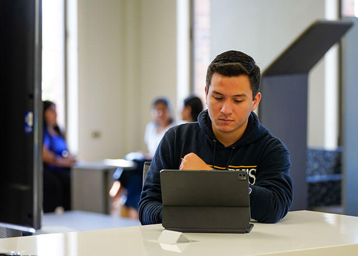 male student in St. Mary's hoodie attends online class on a laptop