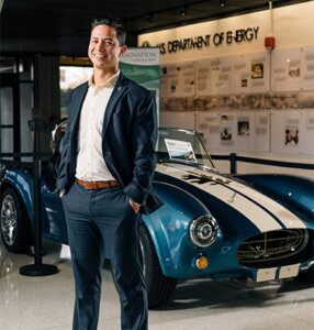 Zack Valdez stands in the U.S. Department of Energy next to its 3D printed, all-electric Shelby Cobra.