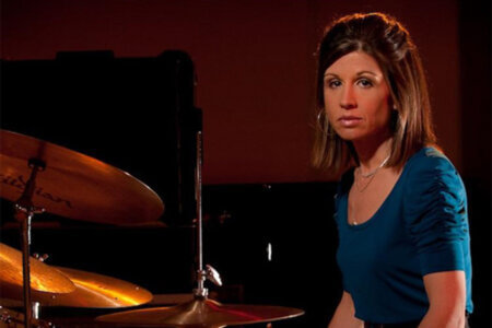 Audra Menconi is seen sitting at a drum kit in a provided photo. 