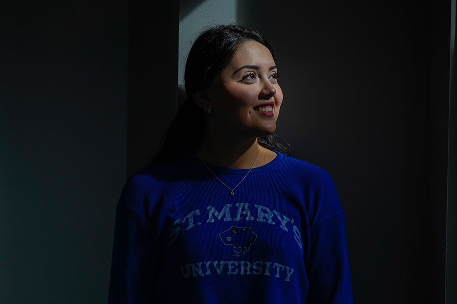 A female student poses for a photo in a dark room. Looking to the right, her face is illuminated.