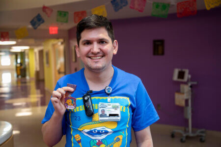 Enrique Salinas became a nurse at CHRISTUS Children's. Here he holds up a Fiesta medal while wearing a Fiesta Oyster Bake T-shirt at the hospital.