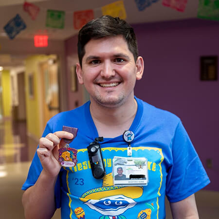 Enrique Salinas became a nurse at CHRISTUS Children's. Here he holds up a Fiesta medal while wearing a Fiesta Oyster Bake T-shirt at the hospital.