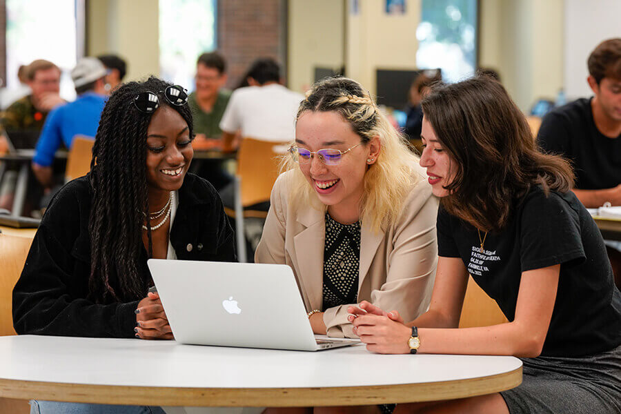 Three students gathered around a table looking at a laptop