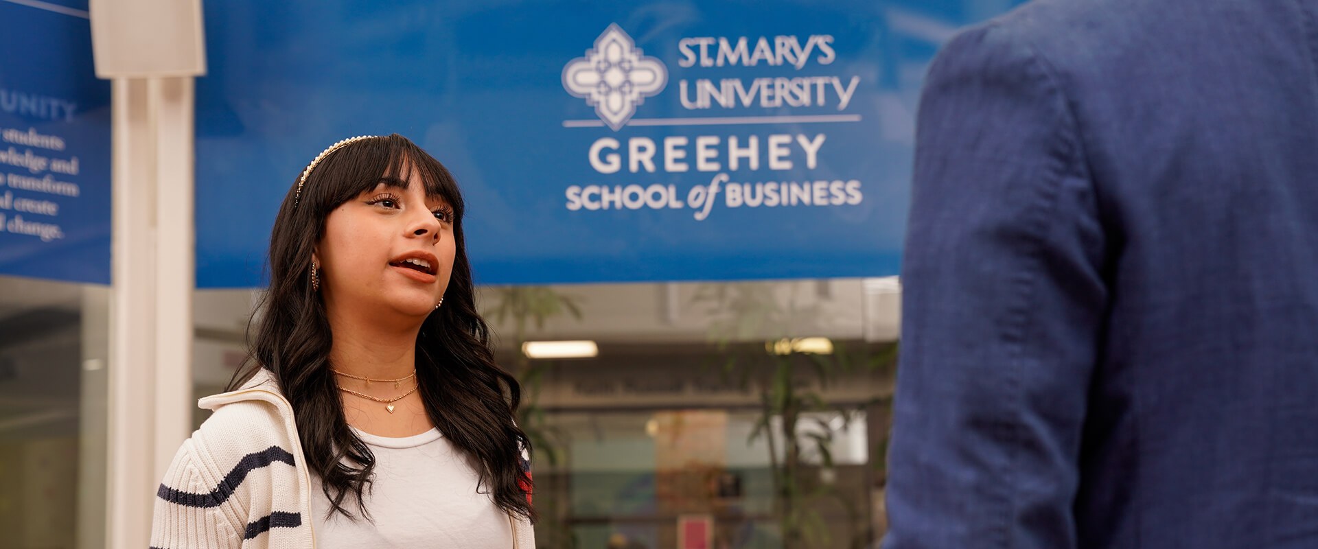 A student speaks to a professor with a Greehey School of Business sign behind her.