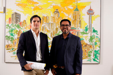 Graduate student Jose Miguel Miranda Garcia and Program Director of Construction Management Juan Pablo Valenzuela talk about the future of construction in front of a painting of the San Antonio skyline. 