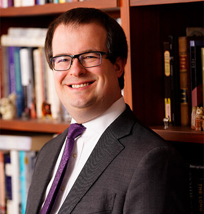 Michael Smith, J.D., St. Mary’s Assistant Professor of Law, stands in front of his bookcase in his office on campus.