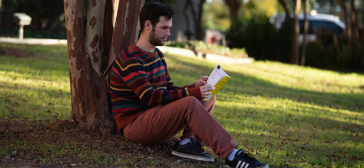 student sitting under a tree and reading