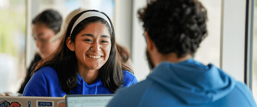 Photo of St. Mary's student smiling at peer wearing St. Mary's University blue sweatshirt and a grey headband
