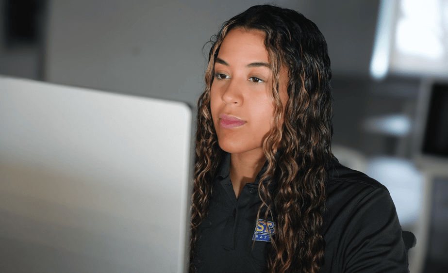 Laurene Robinson wearing a dark gray shirt with the St. Mary's University logo. She sits with her computer.