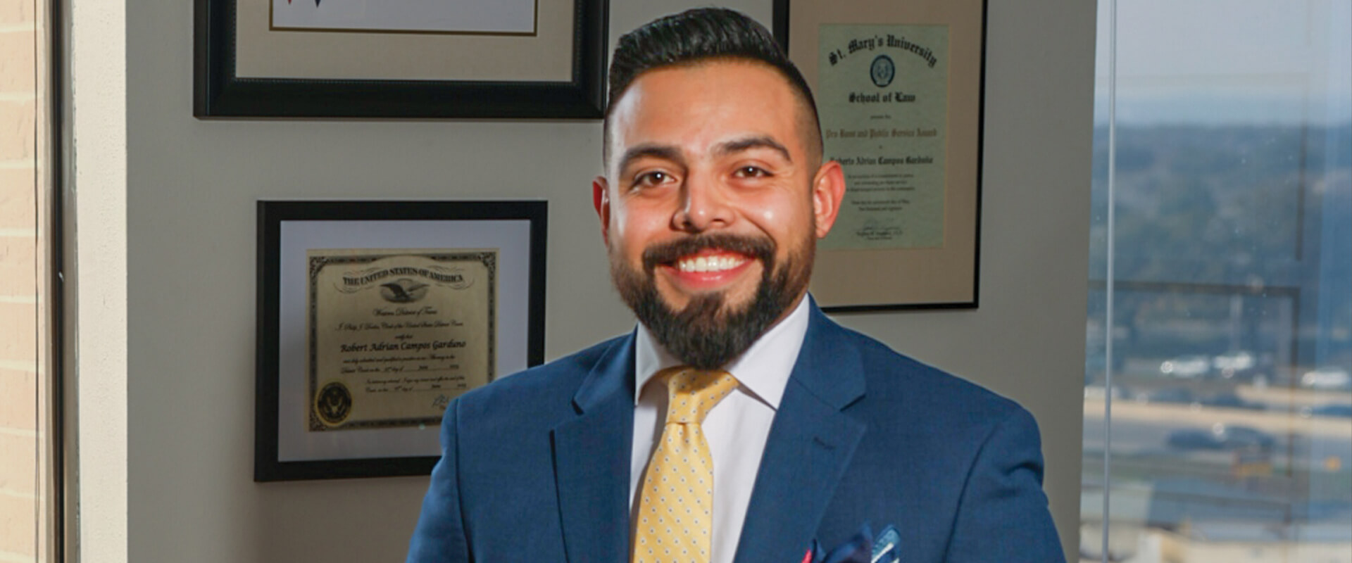 Roberto Campos, who earned his Master of Laws, is in his office. He is wearing a blue suit.
