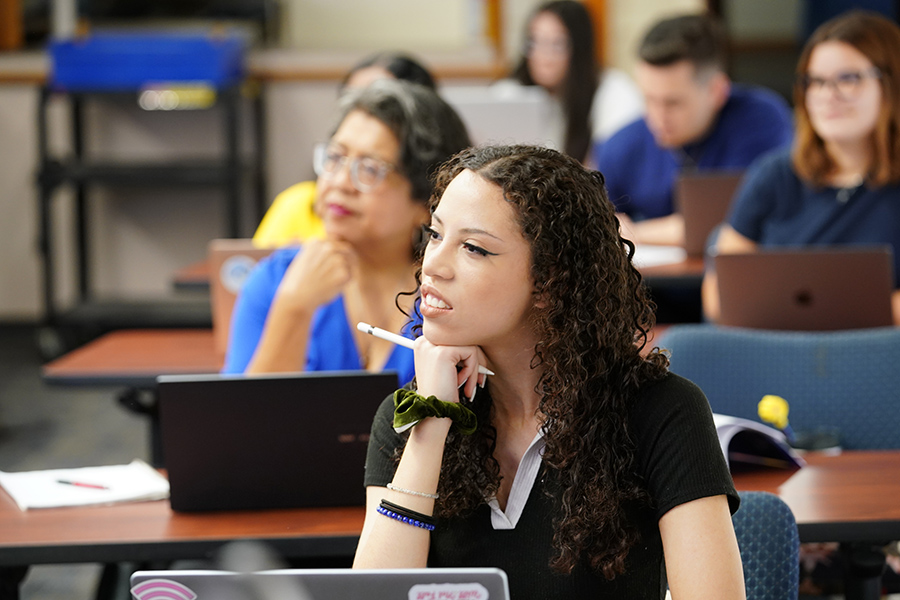 A student sits in a classroom with her chin in her hand, listening to a lecture.