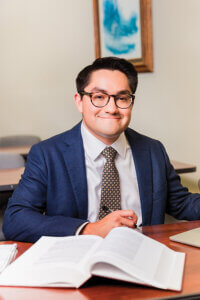 J.D. student Daniel Ramirez in a classroom in the law library. He is wearing a white dress shirt and blue jacket.