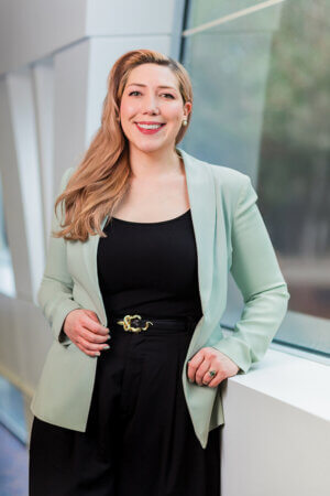 Samantha Alecozay in the law library. She has on black blouse and pants with a green jacket.