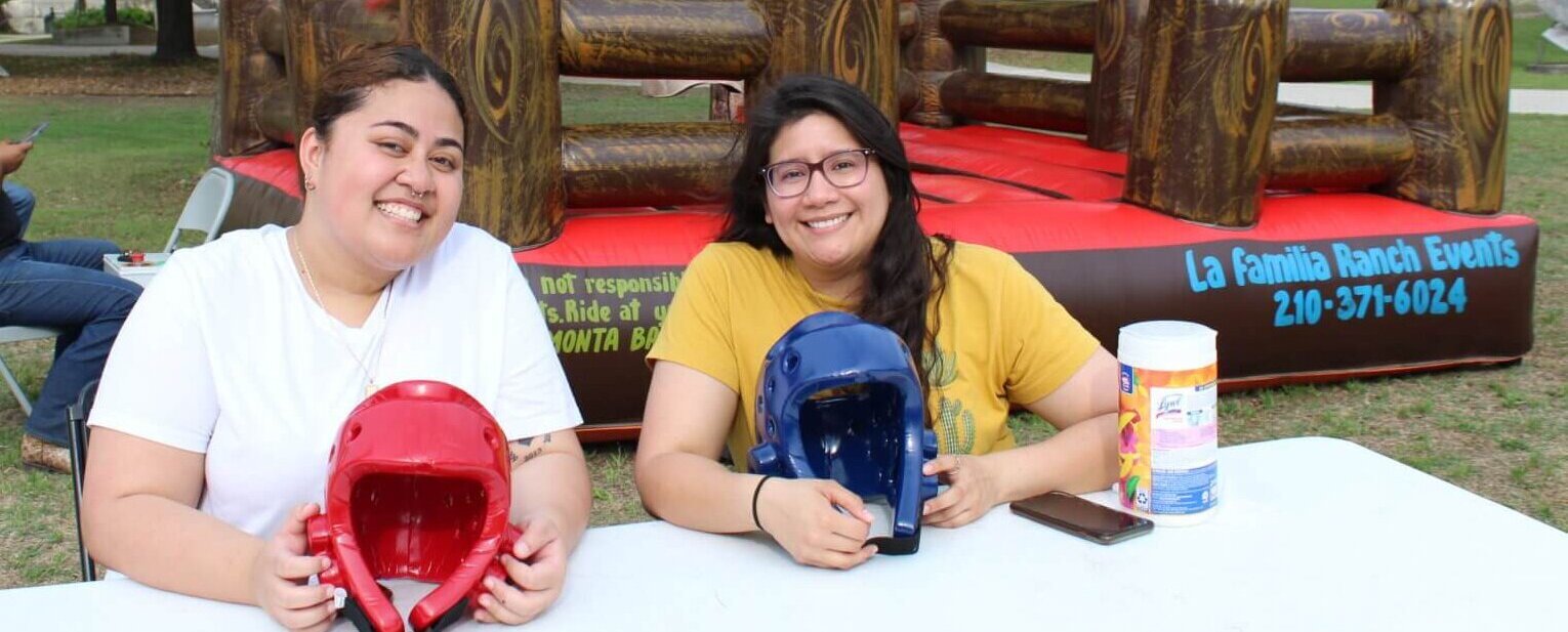 Two female students smile as they hold their helmets preparing for the El Toro Loco ride